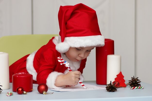 Klein kind in een pak van de kerstman die een brief schrijft met wensen