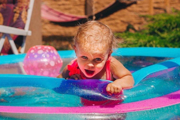 Klein kind in een roze zwempak met één schouder in een opblaasbaar zwembad in de tuin