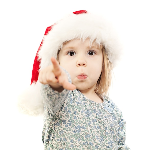Klein kind in kerstmuts wijst met haar vinger op wit. Heb je een cadeau voor me gekocht? Ik wil dit ding!