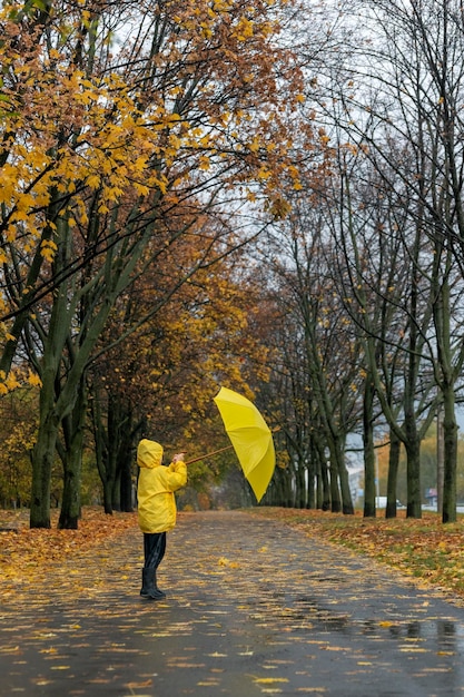 Klein kind loopt in regenachtig park met een gele paraplu in handen Verticaal frame achteraanzicht