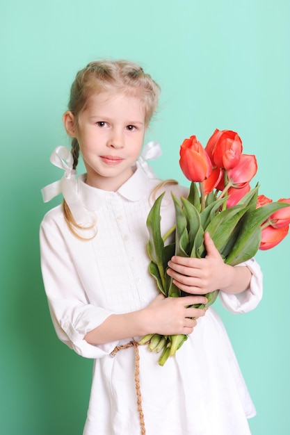 Klein kind meisje met rode tulpen draagt stijlvolle jurk Kijkend naar de camera