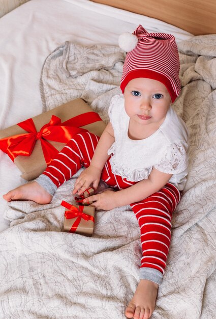 Klein kind met kerstmuts helper zit op het bed met een cadeau