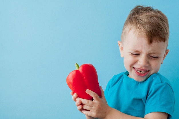 Klein kind met peper in zijn handen op blauwe achtergrond Veganistisch en gezond concept