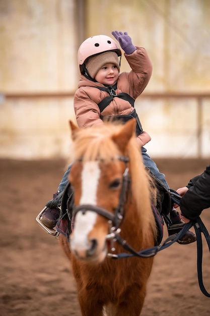 Klein kind rijles drie jaar oud meisje rijdt op een pony en doet oefeningen