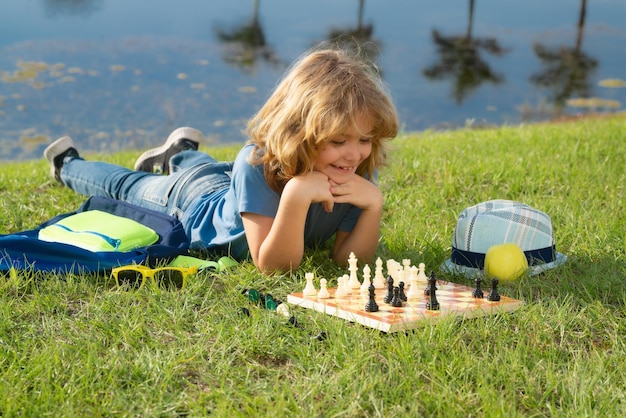 Klein kind schaken in park Kind jongen spelen bordspel buiten Denken kind brainstormen en idee in schaakspel