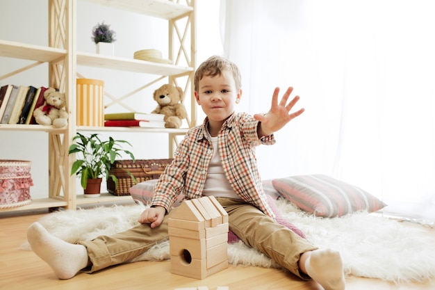 Klein kind zittend op de vloer. Mooie jongen die thuis met houten kubussen speelt. Conceptuele afbeelding met kopie of negatieve ruimte