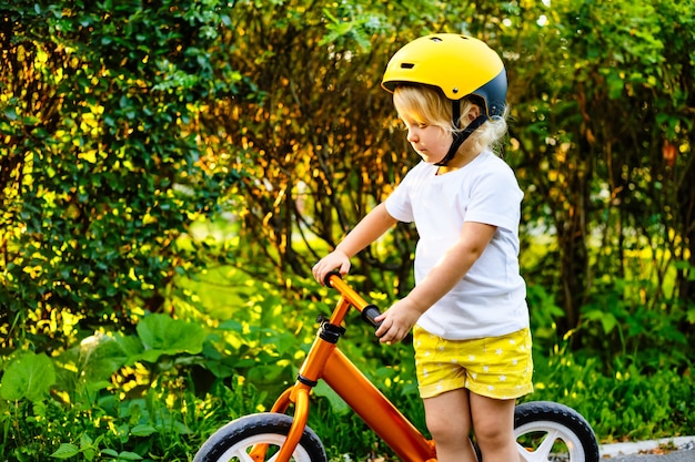 Foto klein kinderenmeisje met helmen en loopfiets die buiten spelen