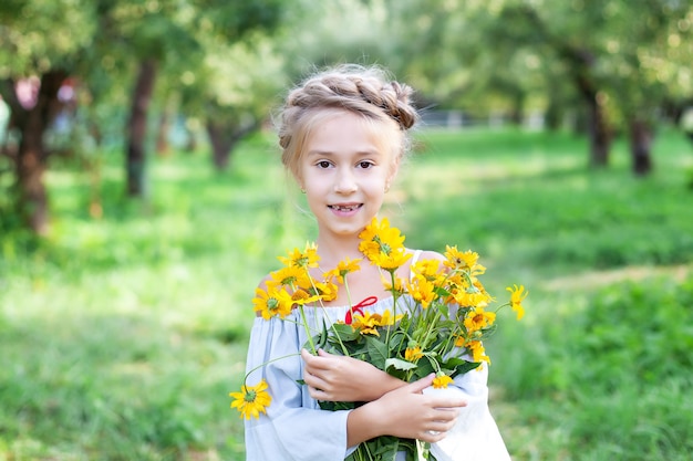 Foto klein lachend blond meisje met een boeket gele bloemen op een achtergrond van tuin