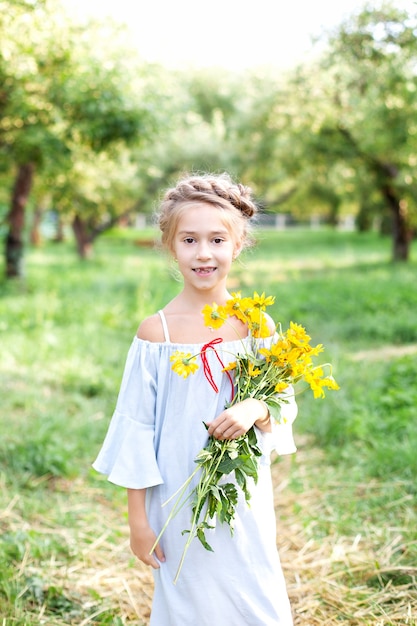 klein lachend blond meisje met een boeket gele bloemen op een achtergrond van tuin