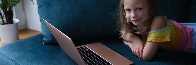 Klein lachend meisje ligt op de bank met laptop close-up