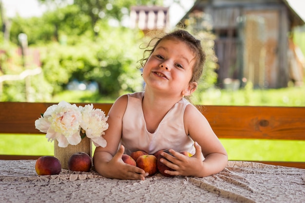 klein meisje aan de tafel met perziken op de natuur in de zomer