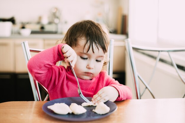 klein meisje aan tafel eet zelf knoedels