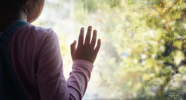 Klein meisje bij raam met regendruppels erop op een regenachtige dag