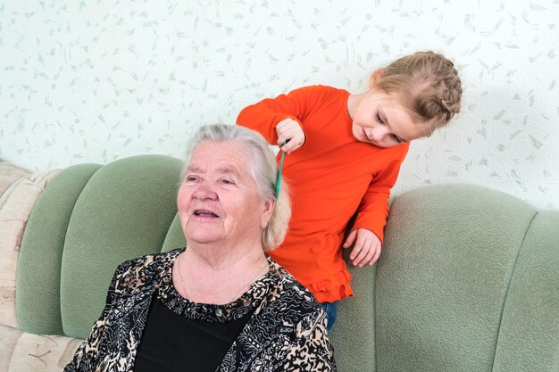 klein meisje borstelt haar overgrootmoederhaar zittend op de bank