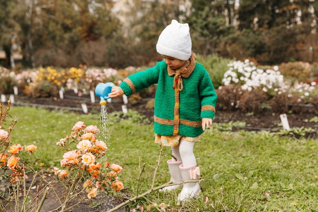 Klein meisje dat bloemen water geeft met een gieter in de tuin