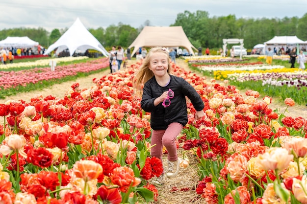 Klein meisje dat door het kleurrijke tulpenveld loopt Kind veel plezier