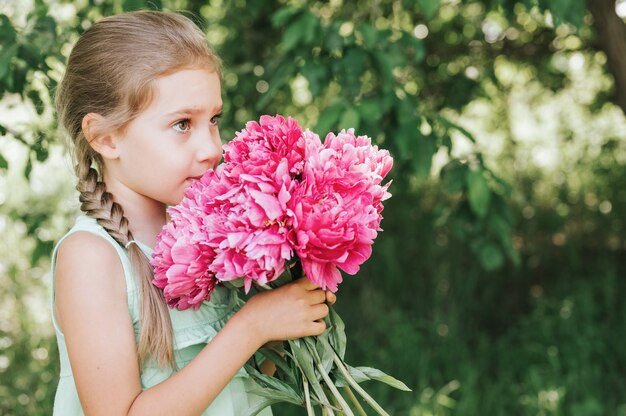 Klein meisje dat een roze pioenroos in haar handen houdt en eraan ruikt