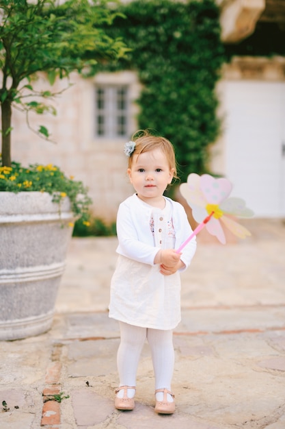 Klein meisje dat een speelgoedbloem in haar handen houdt terwijl ze op de straatstenen tegen de straat staat