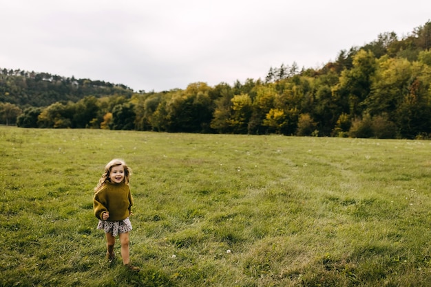 Foto klein meisje dat in een open veld loopt met groen gras met een jurk en een trui aan