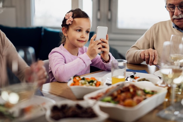 Klein meisje dat mobiele telefoon gebruikt tijdens de lunch met haar grootouders aan de eettafel