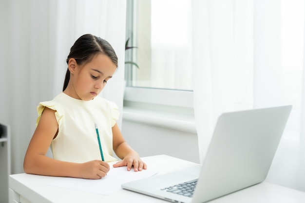 Klein meisje dat naar het scherm van de laptop kijkt met een uitdrukking van verrast en opgewonden. Slim, glimlachend meisje dat aantekeningen maakt. Communicatie in bedrijfsconcept.