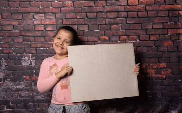 Klein meisje dat poseert met blanco gerecyclede papieren letters voor een oude bakstenen muurachtergrond, donkere achtergrond, selectieve focus.