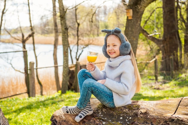 Klein meisje dat 's ochtends sinaasappelsap drinkt in het park buiten in de lente