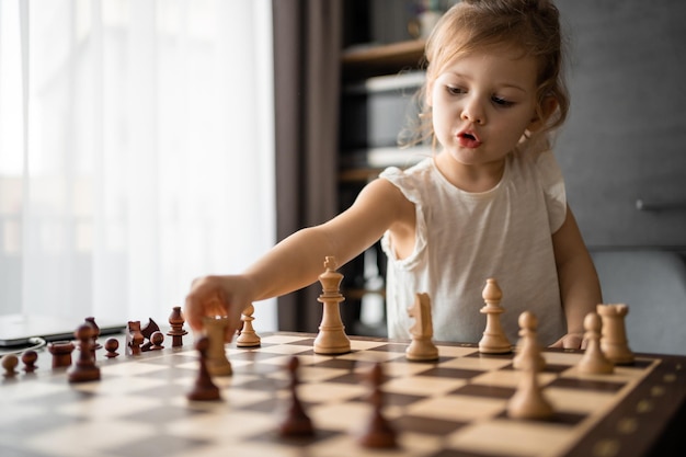 Klein meisje dat schaak speelt aan tafel in de huiskeuken, het concept vroege kinderjarenontwikkeling en e