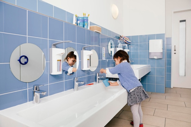 Foto klein meisje dat water gebruikt om haar tanden te poetsen in de badkamer van een kleuterschool