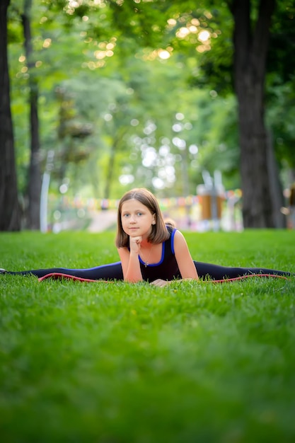 Klein meisje dat yoga doet, zit op het gazon in het park in een touw en kijkt naar de camera