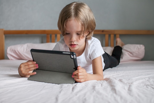 Foto klein meisje doet huiswerk online liggend op het bed thuis communicatie met familieleden online
