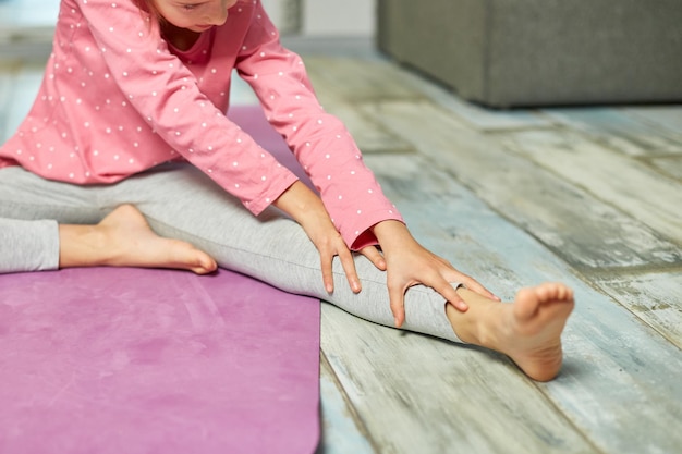 Klein meisje doet rekoefeningen die thuis yoga beoefenen op fitnessmat