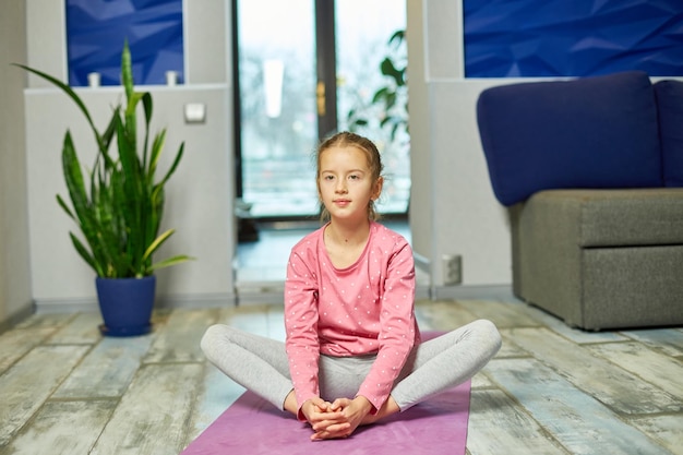 Klein meisje doet rekoefeningen die thuis yoga beoefenen op fitnessmat