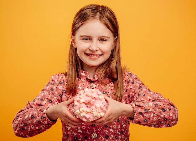 Klein meisje donut houden en kijken naar de camera geïsoleerd op gele achtergrond