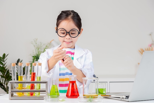 klein meisje Draag een wetenschappelijk grondshirt en werk met een reageerbuiswetenschappelijk experiment in een witte kamer