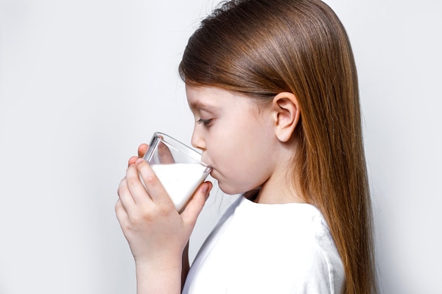 Klein meisje drinkt witte melk uit een transparant glas