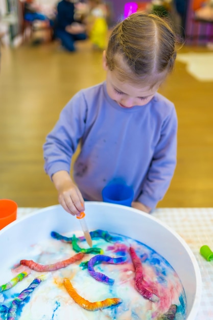 Klein meisje druppelt water op kleurrijke papierwormen sensorische ontwikkeling en ervaart thematische activiteiten