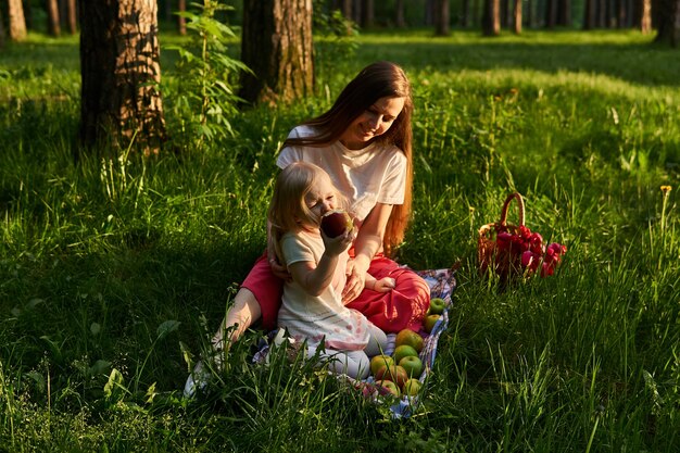 Klein meisje eet een appel in de natuur tijdens een picknick met haar moeder