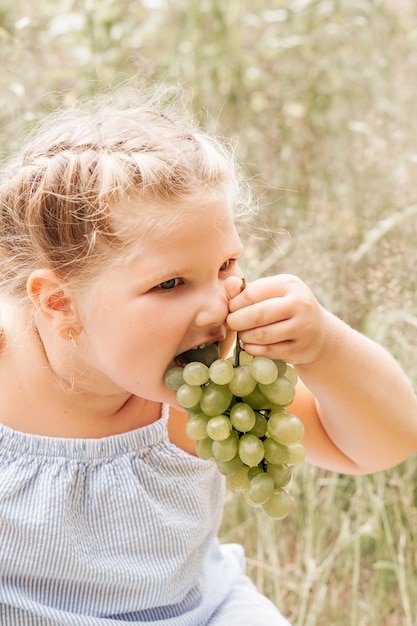 Klein meisje eet in de zomer druiven in de natuur