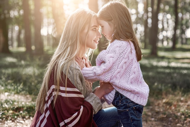 Klein meisje en haar moeder in het herfstpark. Vrouw draagt een stijlvolle muts en gebreide jas, meisje draagt een roze heldere trui
