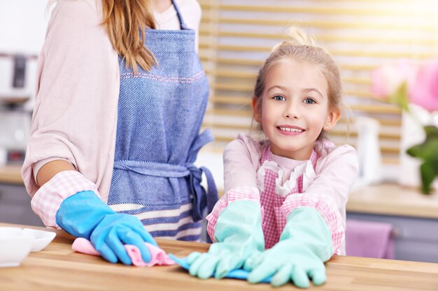 klein meisje en haar moeder in schorten die plezier hebben in het schoonmaken van de keuken