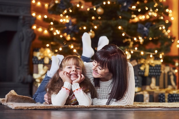 Klein meisje en haar moeder liggen samen op de grond in de met kerst versierde kamer.