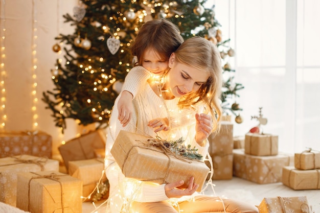 Klein meisje en haar moeder zitten bij de kerstboom en knuffelen