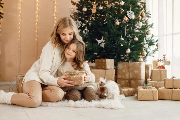 Klein meisje en haar moeder zitten bij de kerstboom met yorkshire terrier