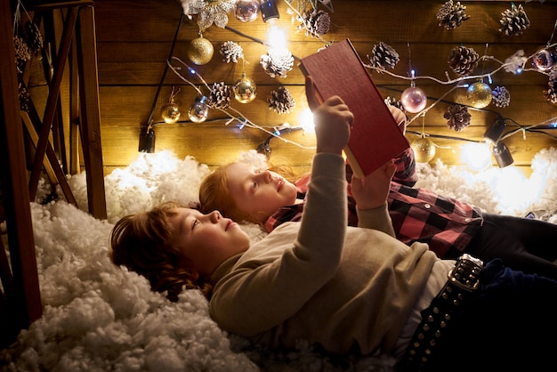 Klein meisje en jongen lezen een boek in een ingerichte kamer voor kerstmis.