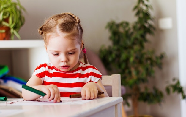 Klein meisje en jongen thuis zitten aan tafel en tekenen met stiften