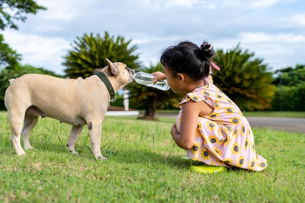 klein meisje geeft haar hond water te drinken op het veld.