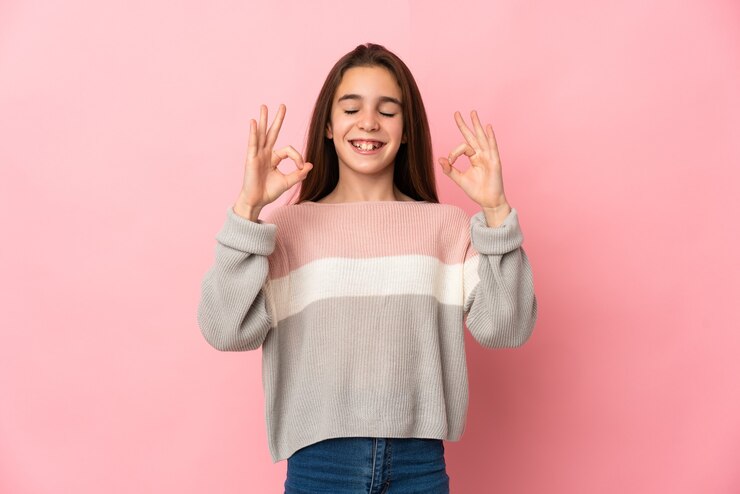 Foto klein meisje geïsoleerd op roze muur in zen pose