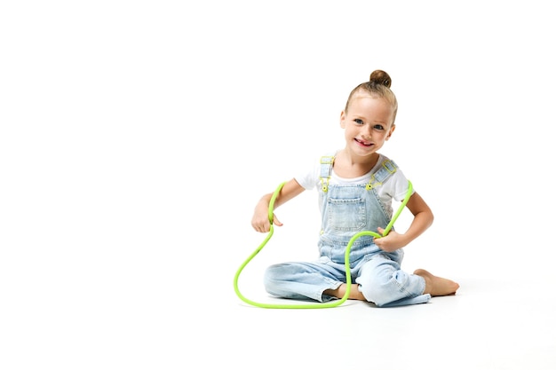Klein meisje gekleed in denim overall met touwtjespringen op een witte achtergrond
