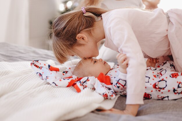 Klein meisje gekleed in pyjama kust haar kleine broertje liggend op het bed.